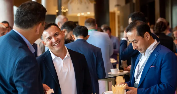 Three business professionals in suits networking and enjoying coffee during a conference reception.